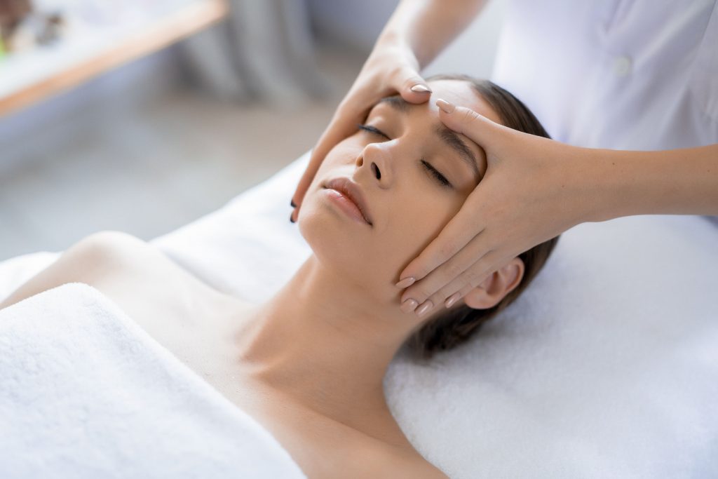 mujer recostada recibiendo masaje en la frente en un spa